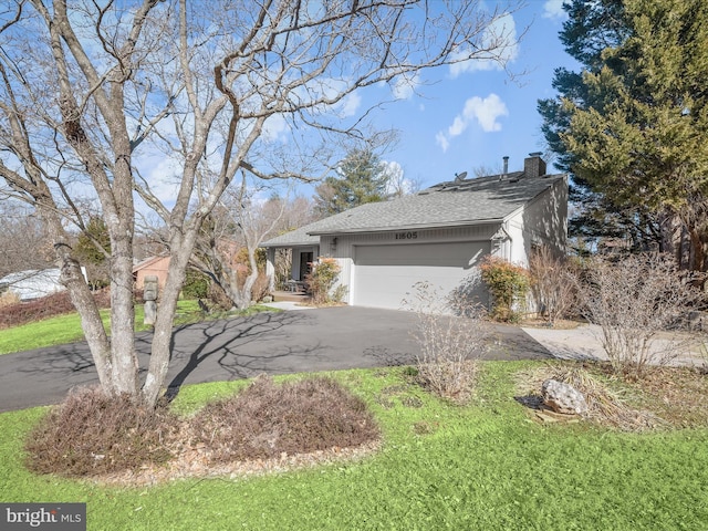 view of side of home featuring aphalt driveway, a chimney, an attached garage, and a shingled roof