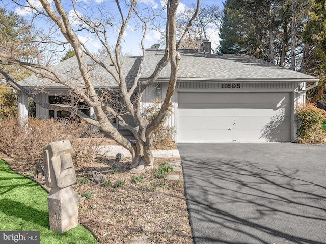 view of front of property with aphalt driveway, roof with shingles, a chimney, and an attached garage