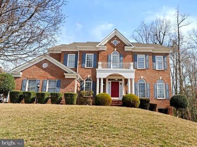 colonial house with a front yard, a balcony, and brick siding