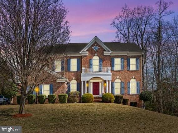 colonial home with a front lawn, a balcony, and brick siding