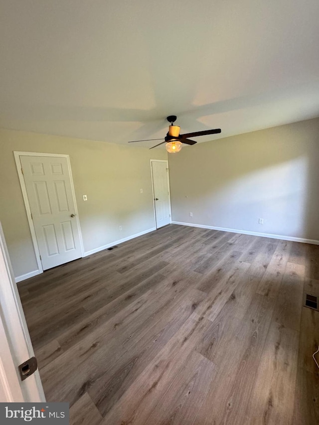 empty room with visible vents, wood finished floors, a ceiling fan, and baseboards