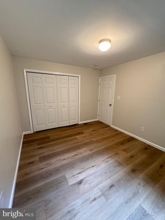 unfurnished bedroom with a closet, wood finished floors, and baseboards