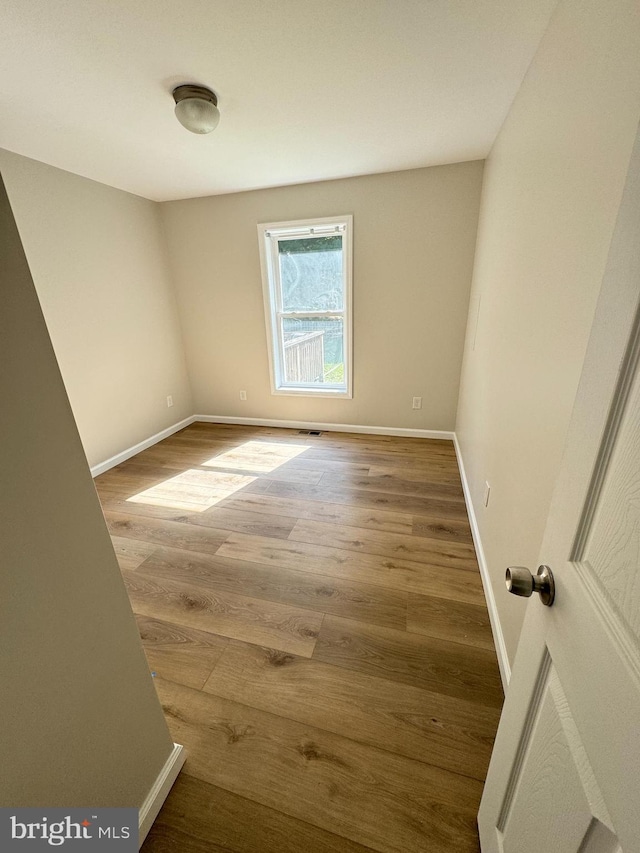 empty room with wood finished floors, visible vents, and baseboards