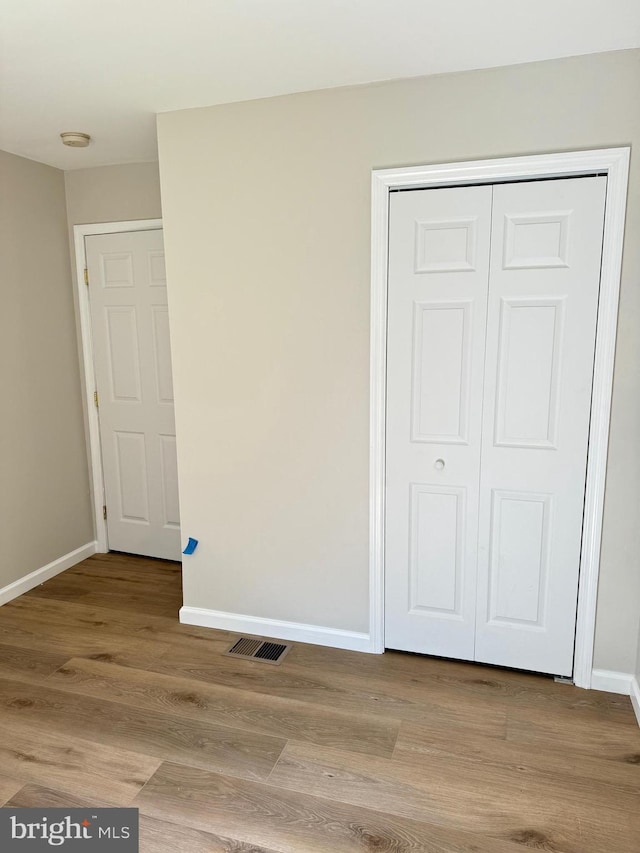 unfurnished bedroom featuring baseboards, a closet, visible vents, and light wood-style floors