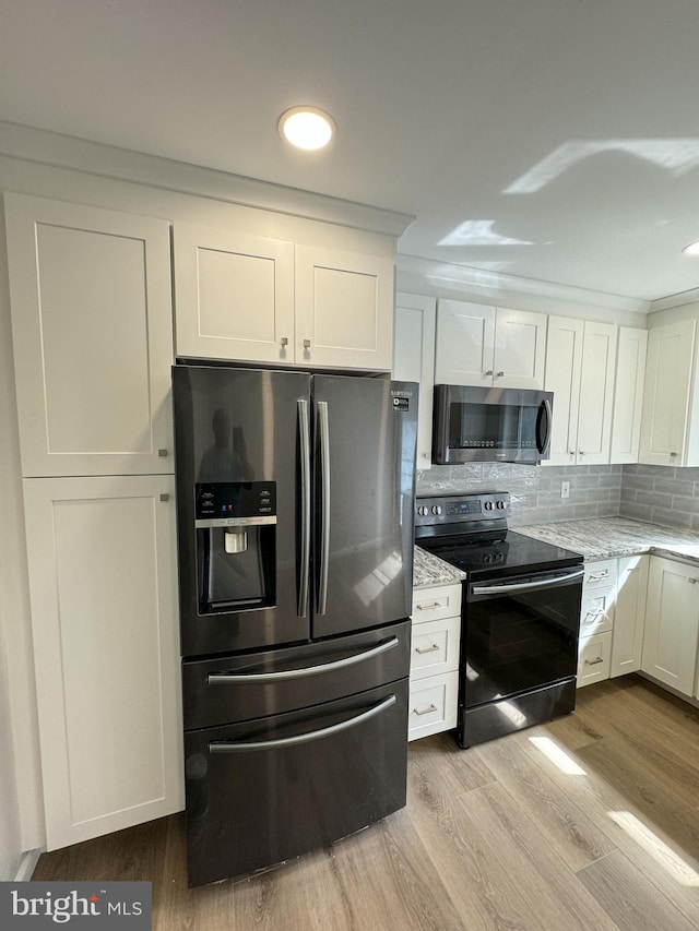 kitchen with appliances with stainless steel finishes, wood finished floors, white cabinetry, and decorative backsplash