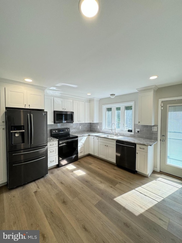 kitchen with light wood-style floors, white cabinetry, a sink, and black appliances