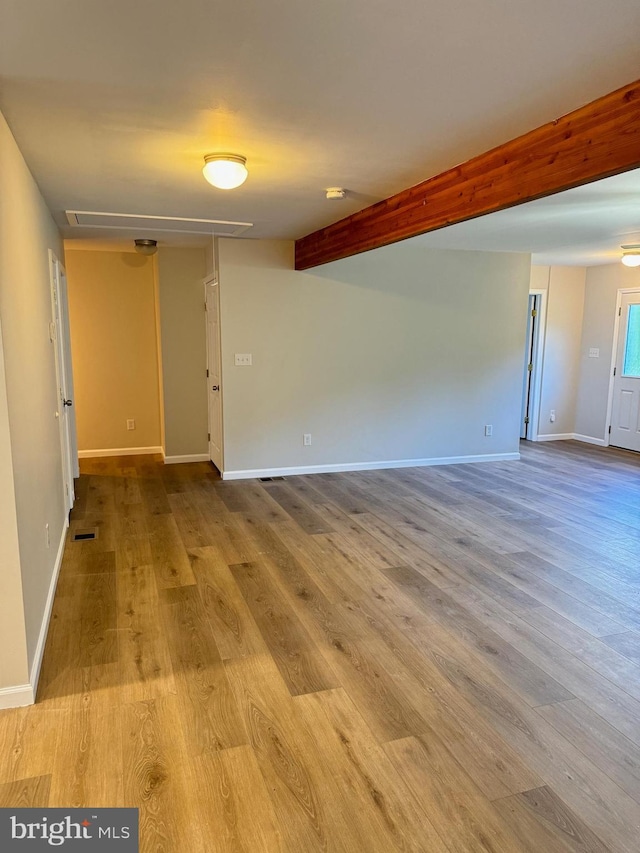 empty room featuring attic access, visible vents, baseboards, beamed ceiling, and wood finished floors