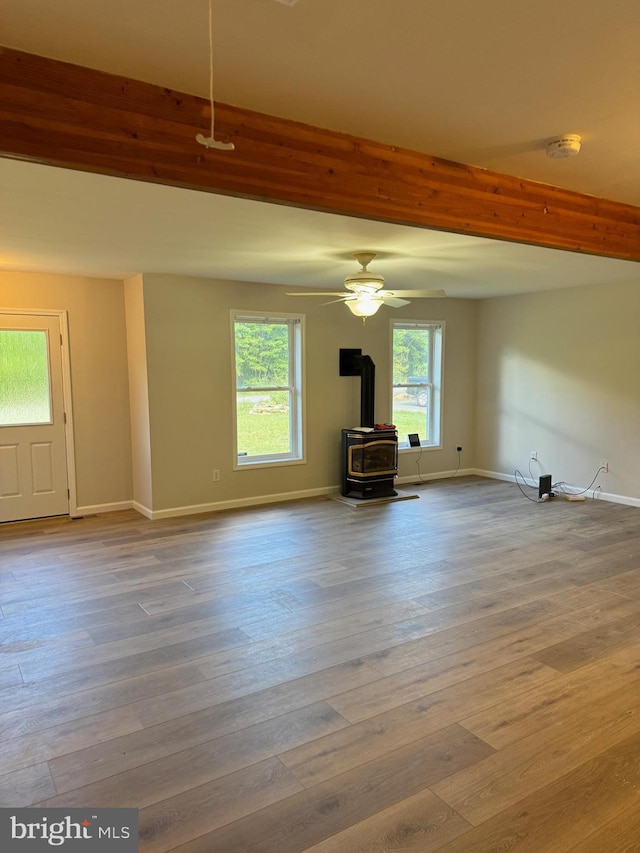 unfurnished living room with a wood stove, baseboards, beam ceiling, and wood finished floors