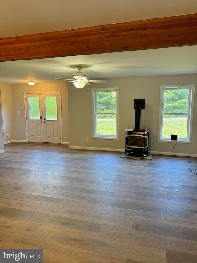 unfurnished living room featuring baseboards, a ceiling fan, wood finished floors, beamed ceiling, and a wood stove