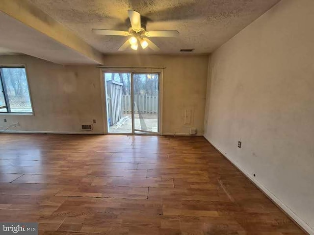 empty room featuring wood-type flooring, visible vents, ceiling fan, and a textured ceiling