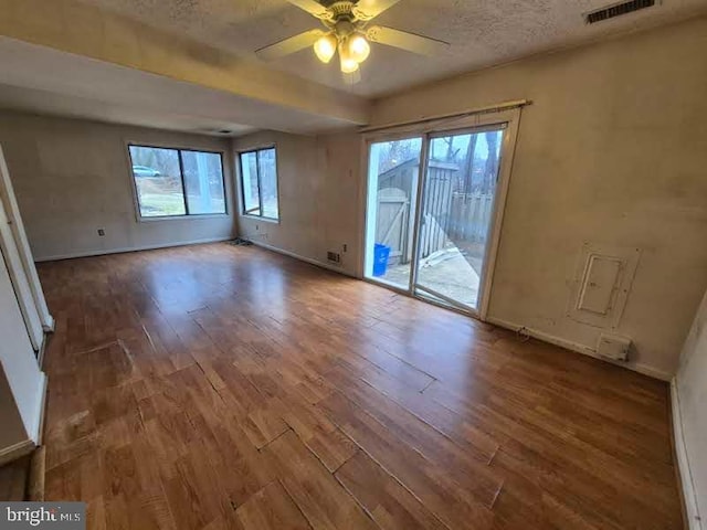 empty room with ceiling fan, a textured ceiling, wood finished floors, visible vents, and baseboards