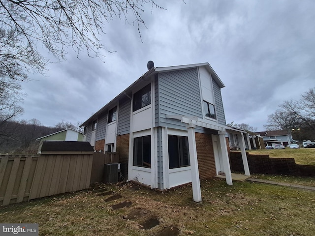 rear view of house featuring brick siding, fence, and central AC unit