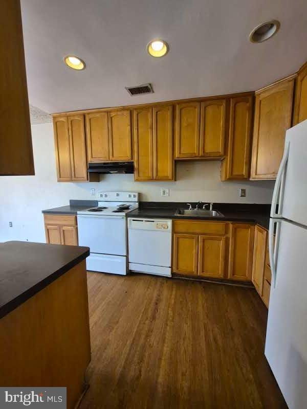 kitchen with white appliances, visible vents, dark countertops, under cabinet range hood, and a sink