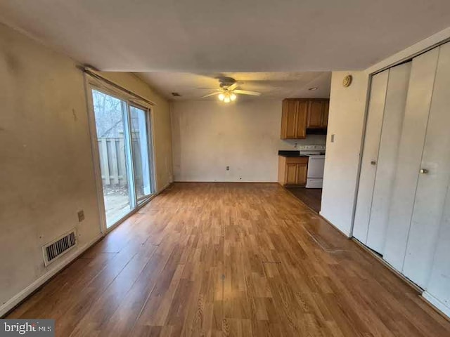 unfurnished living room featuring a ceiling fan, visible vents, baseboards, and wood finished floors