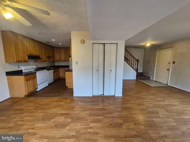 kitchen featuring light wood-type flooring, white appliances, dark countertops, and under cabinet range hood