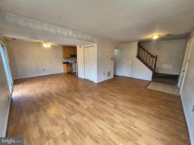 unfurnished living room featuring light wood-style floors, visible vents, ceiling fan, and stairs