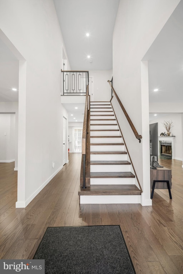 stairs featuring a fireplace, a towering ceiling, baseboards, and wood finished floors