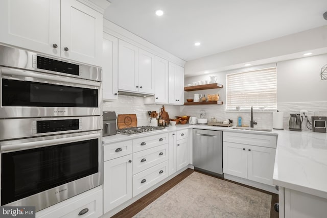 kitchen with stainless steel appliances, decorative backsplash, a sink, and white cabinets