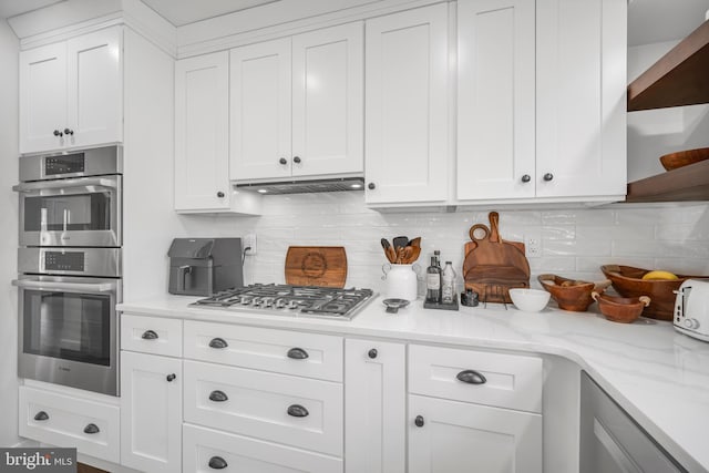 kitchen with stainless steel appliances, open shelves, white cabinetry, and decorative backsplash