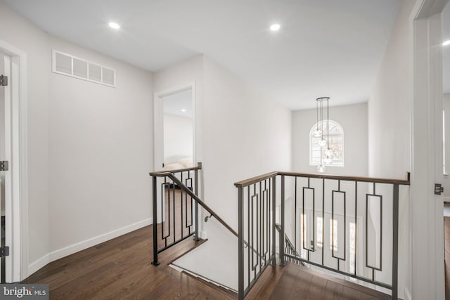 hallway featuring visible vents, an inviting chandelier, an upstairs landing, wood finished floors, and baseboards