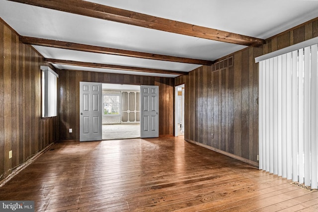 unfurnished room with visible vents, beamed ceiling, wooden walls, and hardwood / wood-style flooring