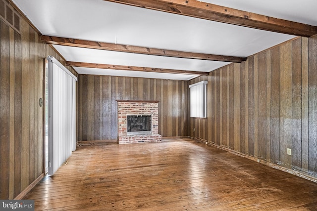 unfurnished living room with beam ceiling, a fireplace, wooden walls, and hardwood / wood-style floors