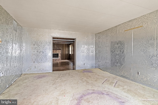 carpeted empty room with a brick fireplace and wallpapered walls