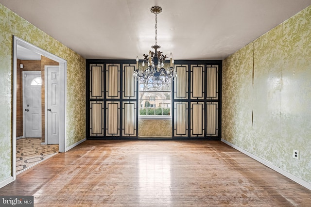 unfurnished dining area featuring a notable chandelier, baseboards, light wood-style flooring, and wallpapered walls