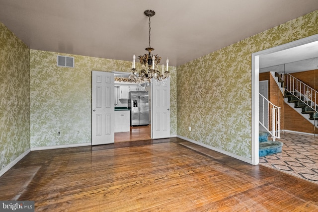 unfurnished dining area with wallpapered walls, visible vents, dark wood-type flooring, stairs, and a chandelier