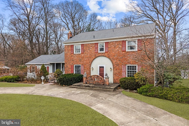 view of front facade featuring roof with shingles, a front yard, a chimney, and brick siding