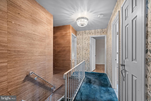 hallway with wood finished floors, an upstairs landing, and wallpapered walls