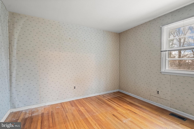 empty room featuring visible vents, light wood-style flooring, baseboards, and wallpapered walls