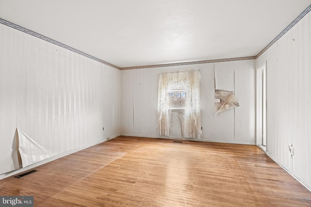 empty room with visible vents, wood finished floors, and ornamental molding