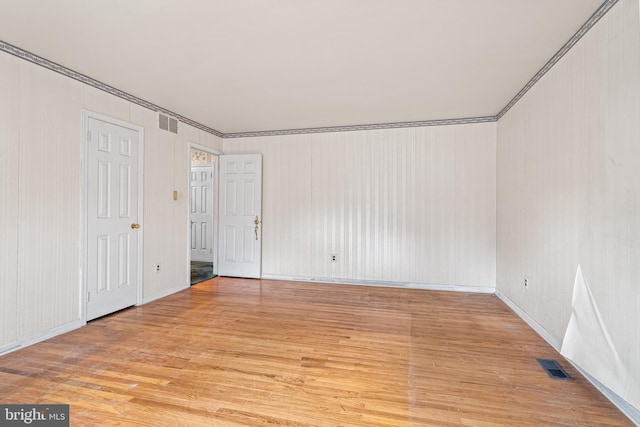 empty room with light wood-style floors, visible vents, crown molding, and baseboards