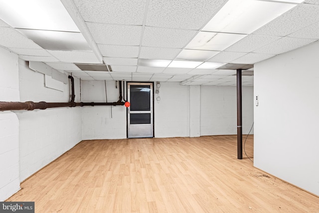 finished below grade area featuring concrete block wall, a paneled ceiling, and light wood finished floors