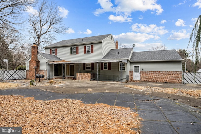 rear view of house with roof with shingles, fence, a chimney, and brick siding