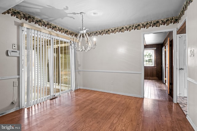 unfurnished dining area with a notable chandelier, baseboards, and wood finished floors