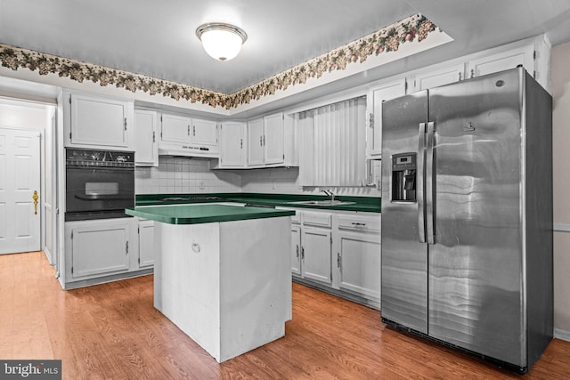 kitchen with dark countertops, a sink, stainless steel fridge, oven, and under cabinet range hood