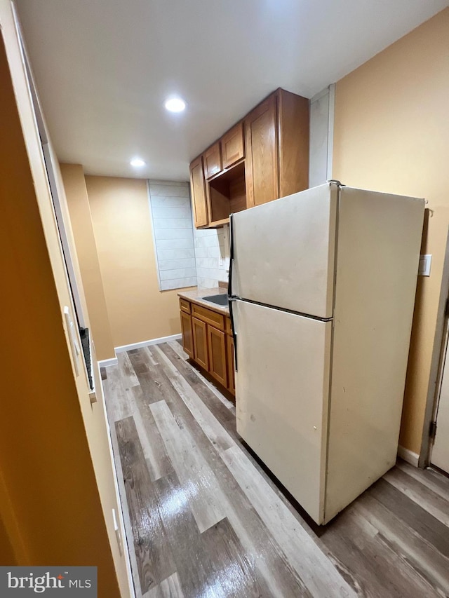 kitchen with light wood-style floors, brown cabinets, decorative backsplash, and freestanding refrigerator