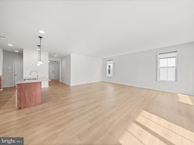 unfurnished living room with light wood finished floors, plenty of natural light, a sink, and visible vents