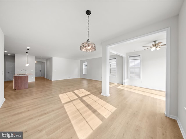 unfurnished living room featuring ceiling fan, baseboards, a sink, and light wood-style floors