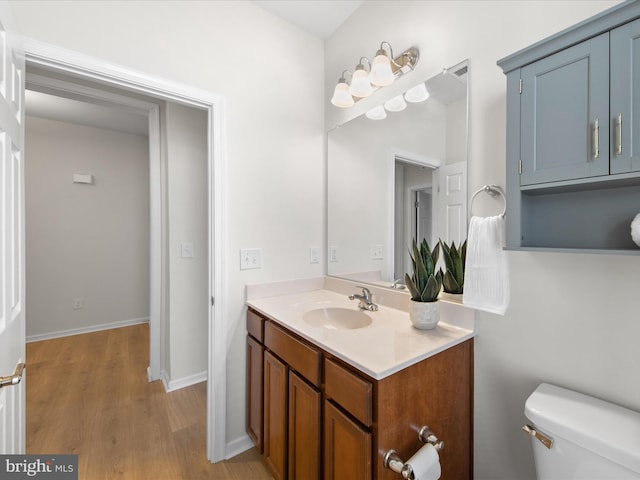 half bath featuring baseboards, visible vents, toilet, wood finished floors, and vanity