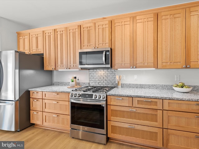 kitchen featuring light stone countertops, light wood-style flooring, appliances with stainless steel finishes, and backsplash