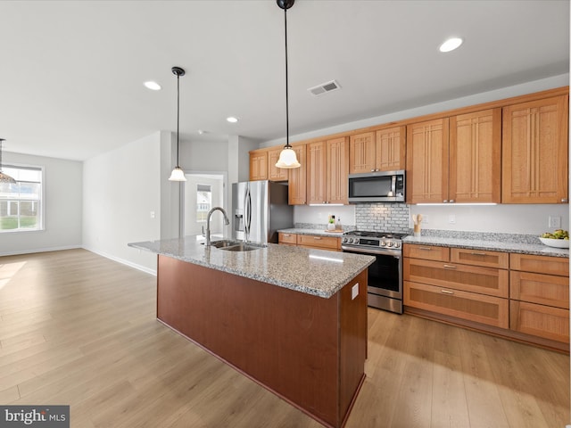 kitchen with light wood-style flooring, stainless steel appliances, a sink, visible vents, and an island with sink