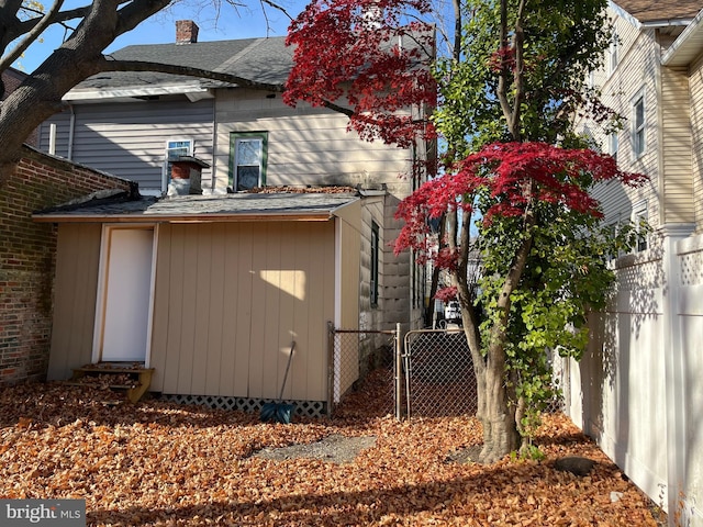 view of home's exterior featuring a shingled roof, a gate, fence, and a chimney