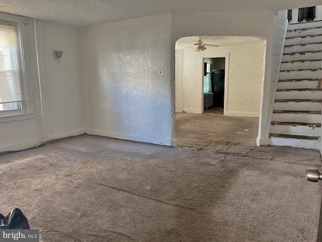 carpeted spare room with a textured ceiling, a textured wall, and a ceiling fan