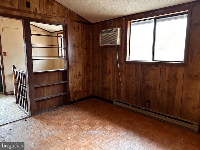 empty room featuring a wall unit AC, a baseboard radiator, vaulted ceiling, wooden walls, and a textured ceiling