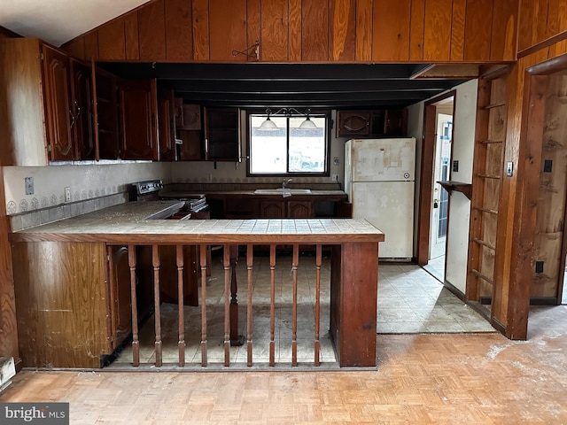 kitchen featuring tile countertops, a sink, vaulted ceiling, range, and freestanding refrigerator