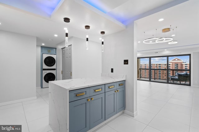 kitchen with light stone counters, light tile patterned flooring, a peninsula, stacked washer / dryer, and hanging light fixtures