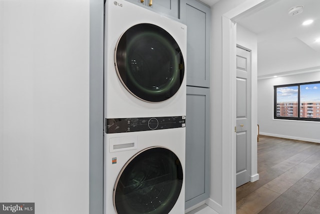 laundry area with recessed lighting, cabinet space, stacked washer / dryer, wood finished floors, and baseboards